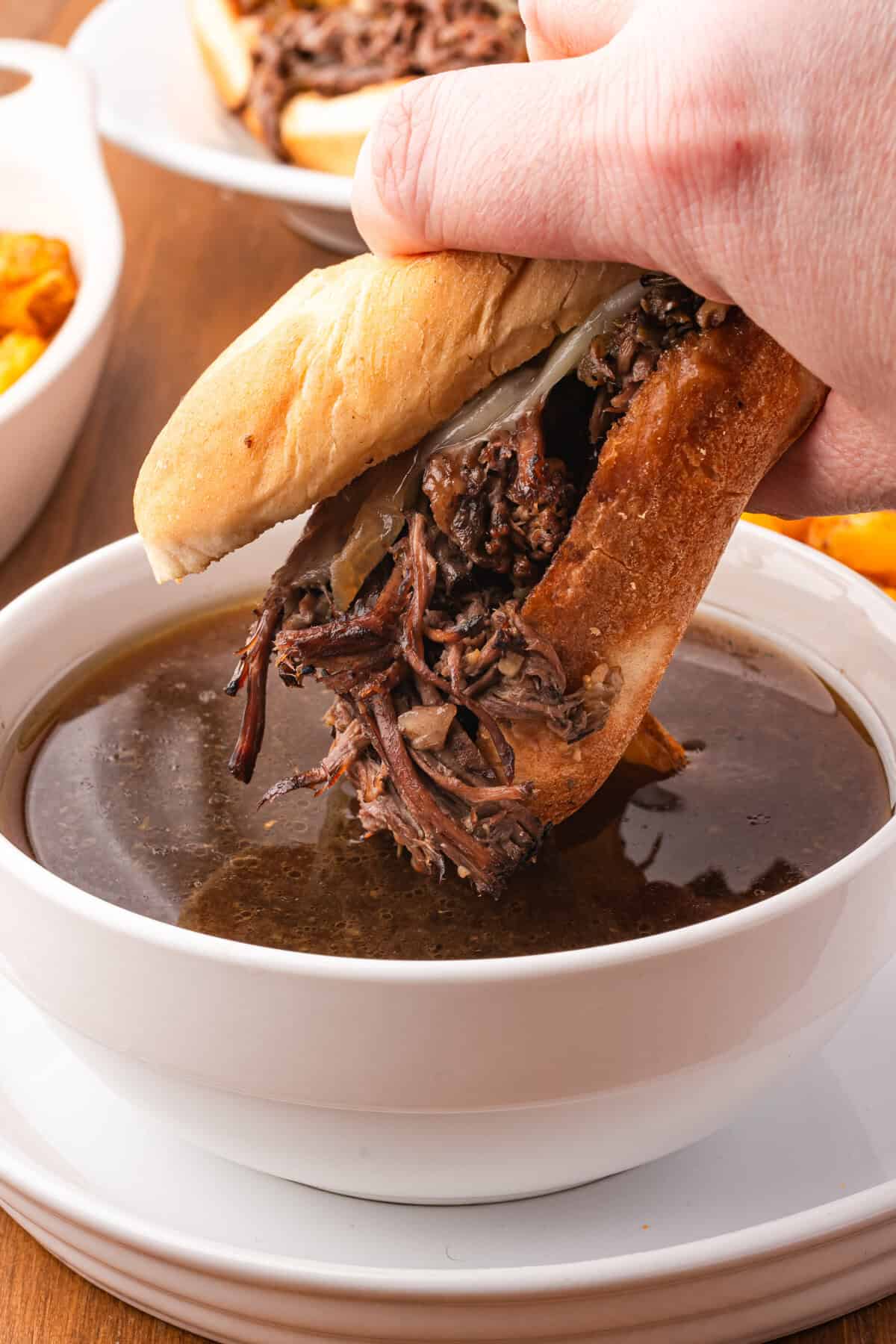 A French Dip Sandwich being dunked into beef au jus.