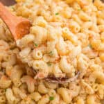 A wooden spoon lifting a scoop of creamy Hawaiian mac salad with shredded carrots and green onion from a bowl.