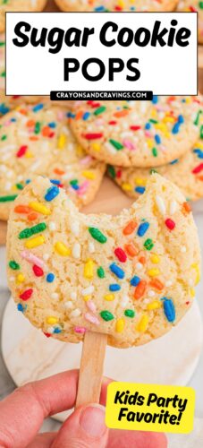A hand holding a sprinkle sugar cookie on a stick with a bite taken out, more cookies behind. Overlay text: Sugar Cookie Pops, crayonsandcravings.com, Kids Party Favorite!