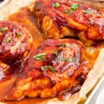 Baked BBQ chicken breasts on a parchment-lined sheet pan.