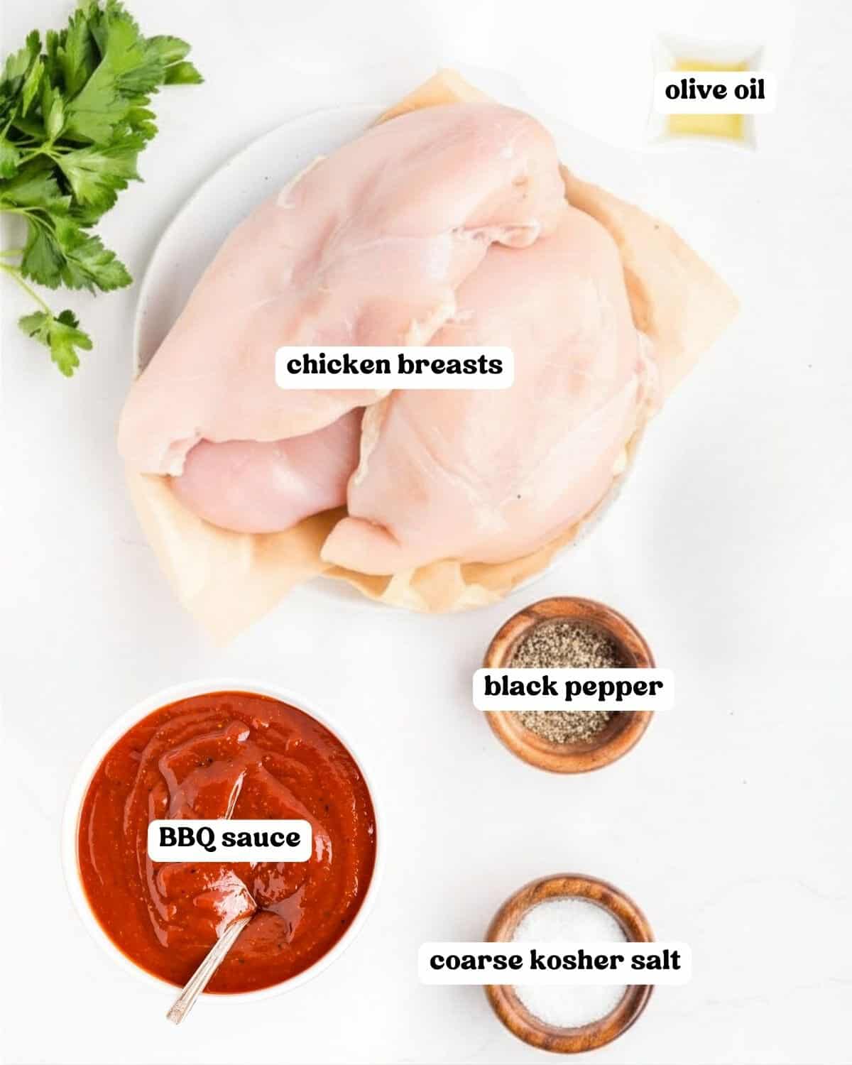 Labeled ingredients on a white counter: chicken breasts, olive oil, BBQ sauce, black pepper, coarse salt, and parsley.