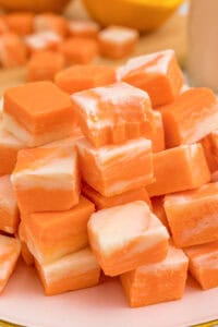 A pile of orange and white swirled fudge squares stacked on a pink plate.