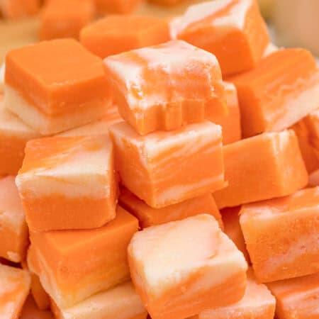 A pile of orange and white swirled fudge squares stacked on a pink plate.