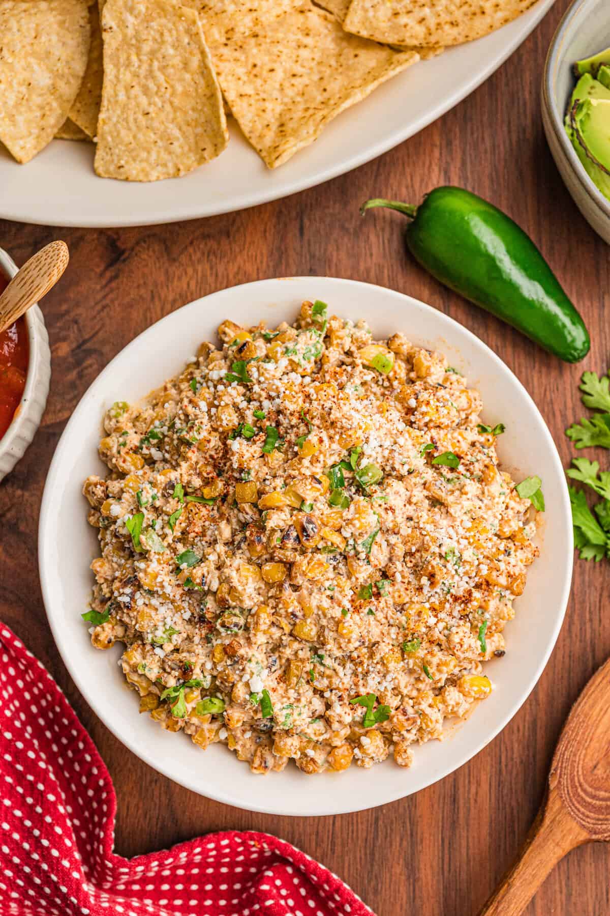 Overhead view of easy street corn dip in a white bowl topped with cotija and chili powder, chips alongside.