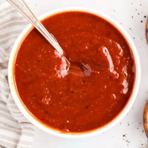 Overhead view of homemade BBQ sauce in a white bowl with a spoon resting in it.