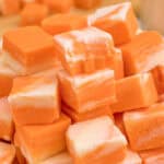 A pile of orange and white swirled fudge squares stacked on a pink plate.