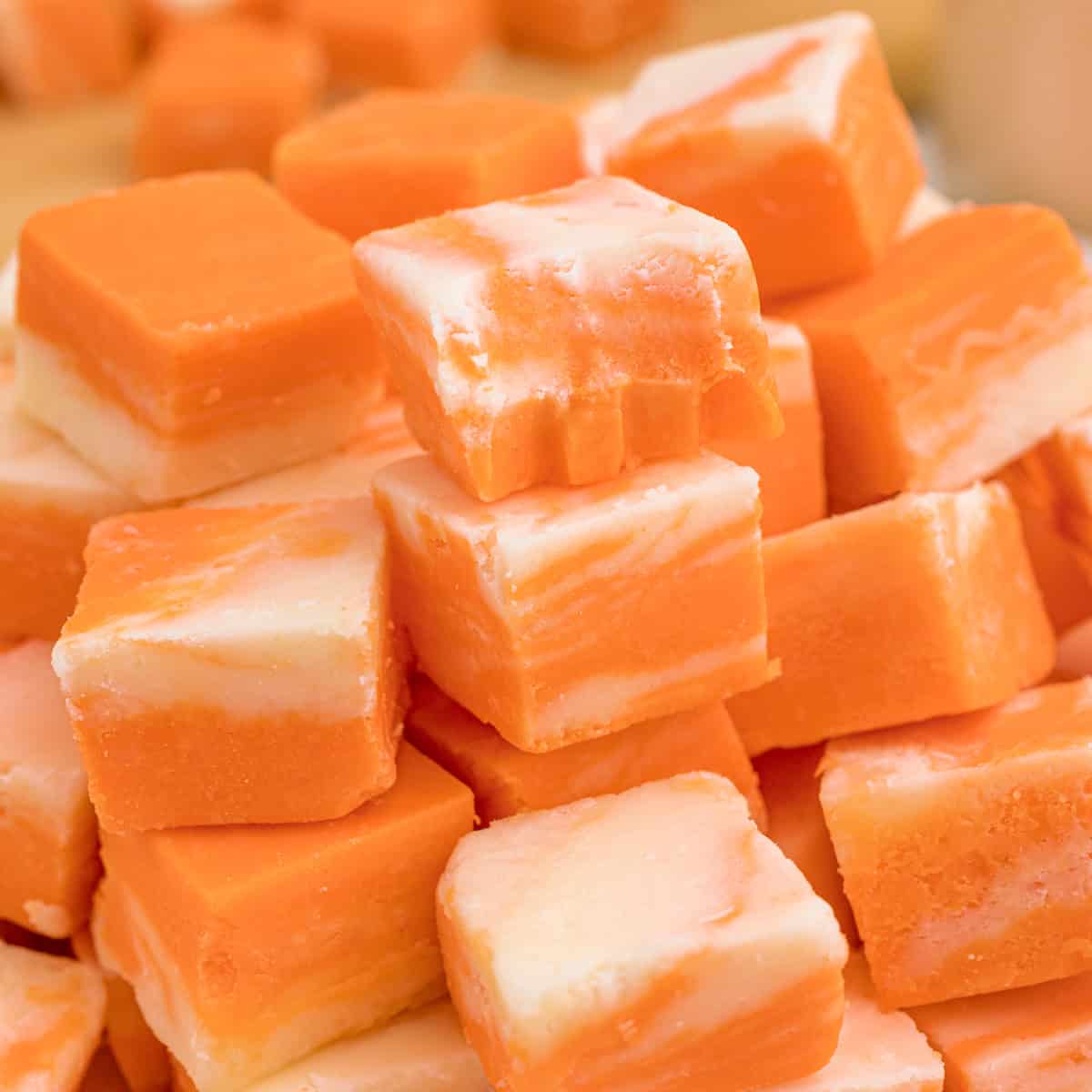 A pile of orange and white swirled fudge squares stacked on a pink plate.