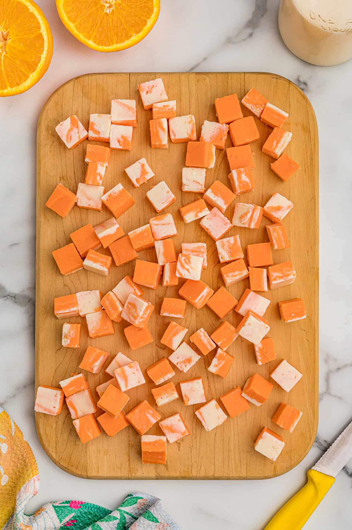 Orange creamsicle fudge cut into cubes on a wood board with orange halves and a knife nearby.