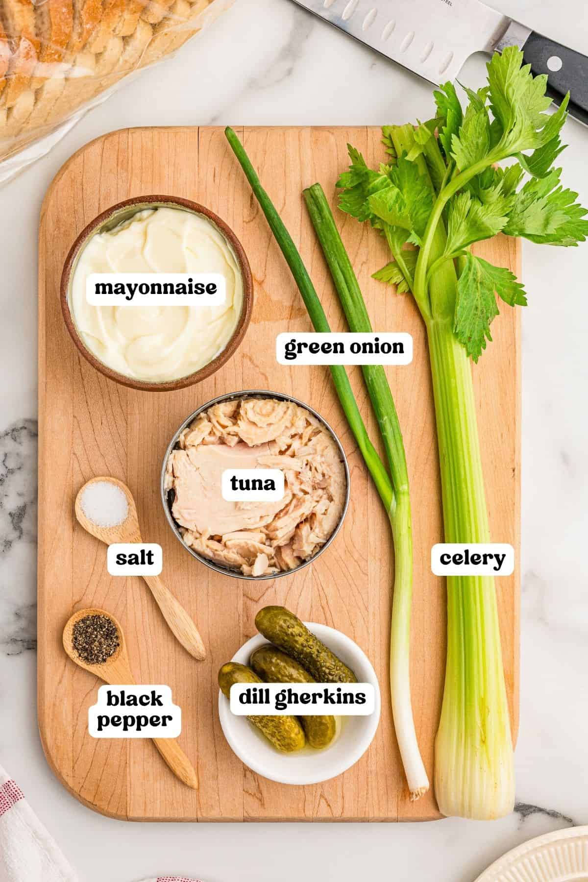 Ingredients on a wooden board: mayonnaise, canned tuna, green onion, celery, dill gherkins, salt, and black pepper.