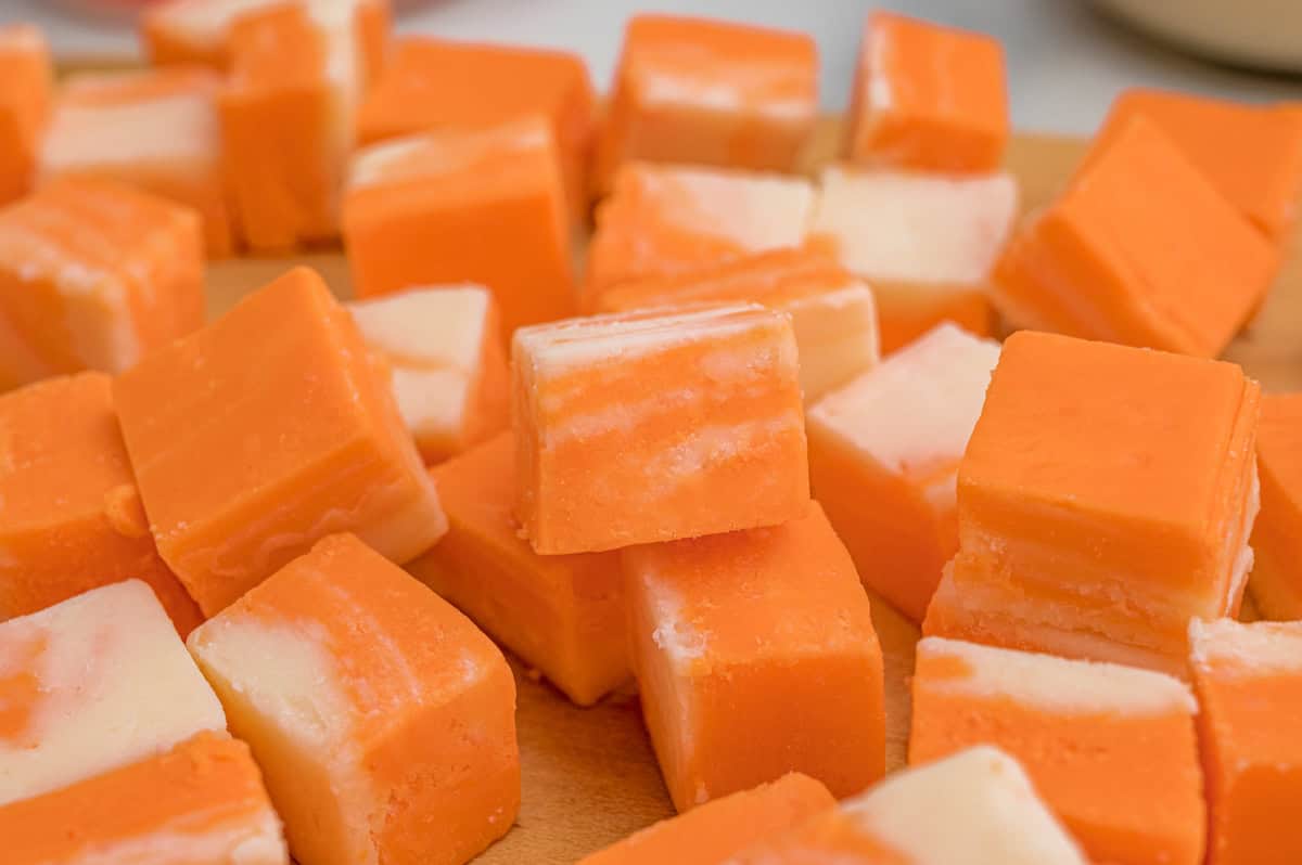 Close-up of orange and white fudge squares scattered on a wood cutting board.
