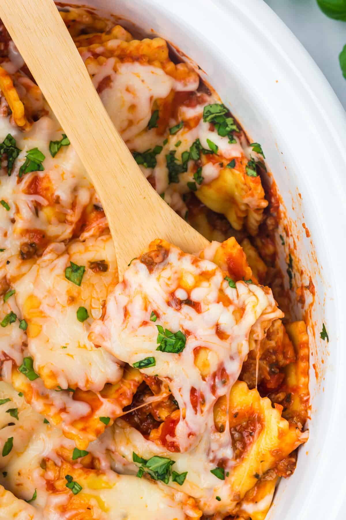 Cheesy crockpot ravioli lasagna topped with basil with a wooden spoon.