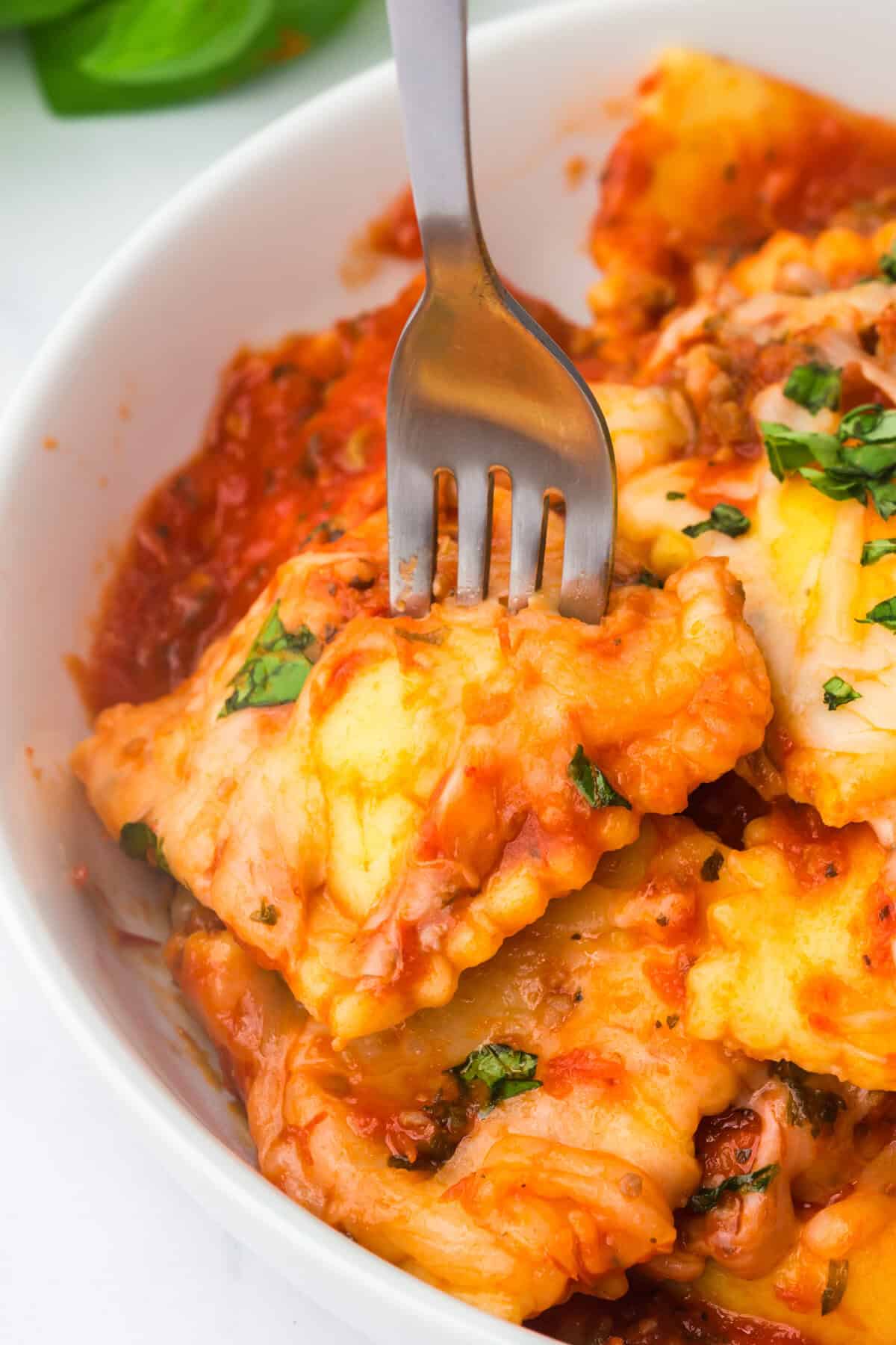 Crockpot ravioli lasagna in a white bowl topped with melted mozzarella and chopped fresh basil.