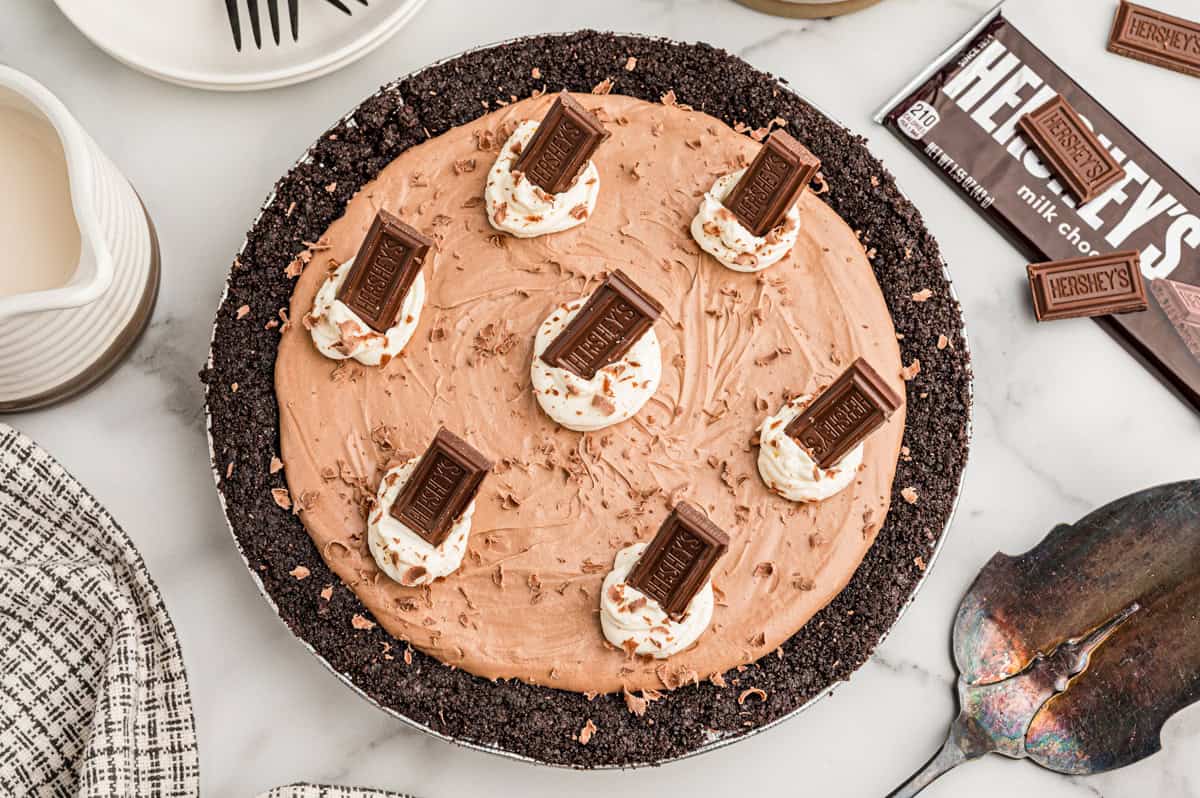 Overhead view of a whole chocolate pie in an Oreo crust topped with whipped cream and Hershey's bars.