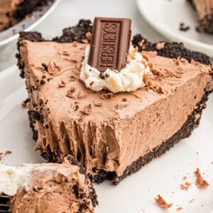 A slice of Hershey pie with an Oreo crust, topped with whipped cream, a Hershey's bar, and chocolate shavings.