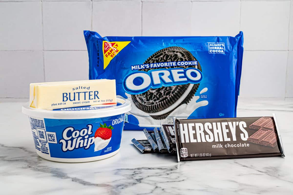 Ingredients on a marble counter: Oreo cookies, salted butter, a tub of Cool Whip, and Hershey's milk chocolate bars.