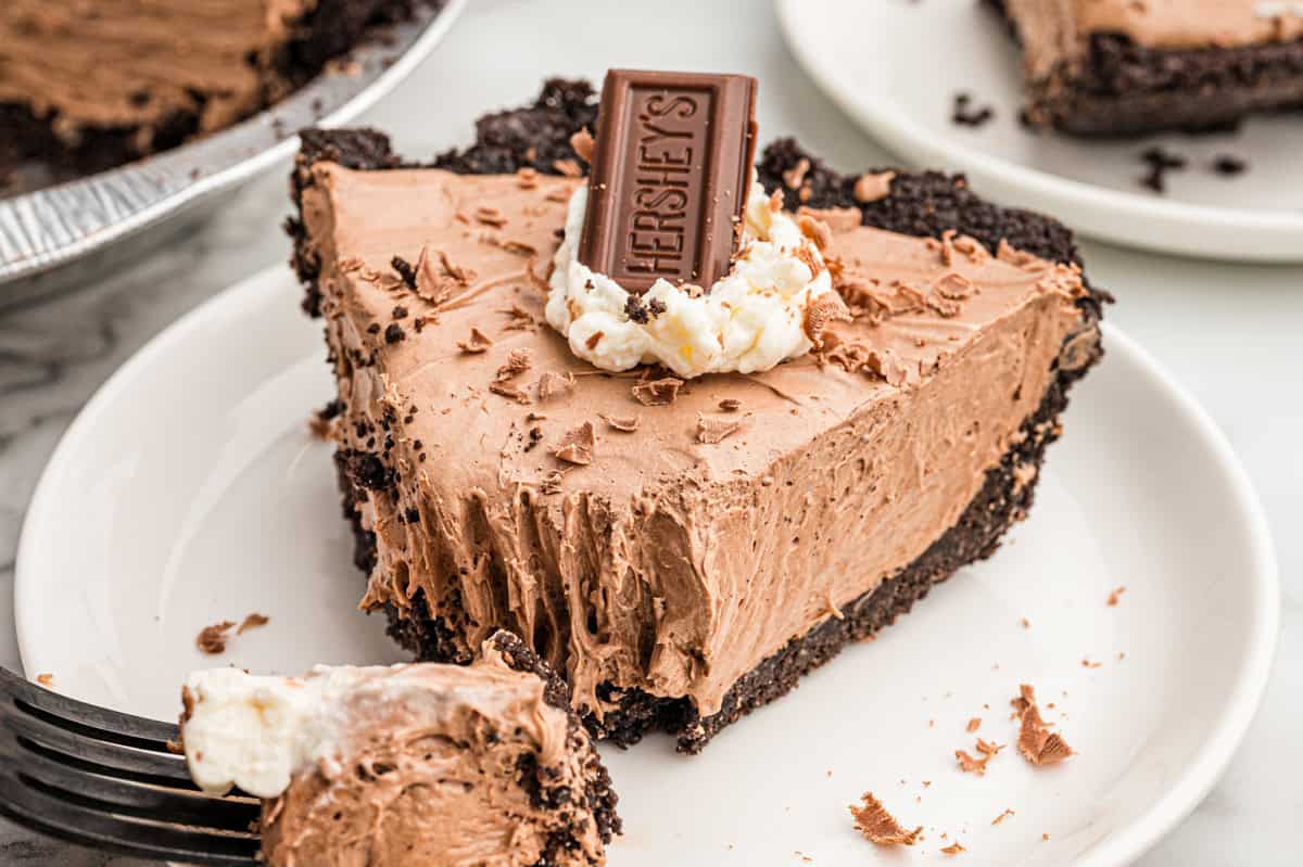 A slice of no bake chocolate pie on a white plate with a forkful on a fork at the edge of the frame.