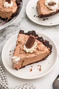 A slice of chocolate pie on a white plate with a second plated slice and the pie behind it.