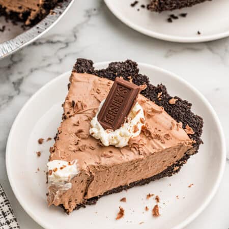 A slice of chocolate pie on a white plate with a second plated slice and the pie behind it.