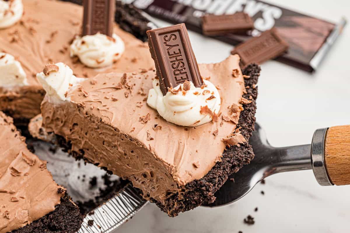 A slice of pie lifted on a pie server, with Hershey's bars and the rest of the pie behind.