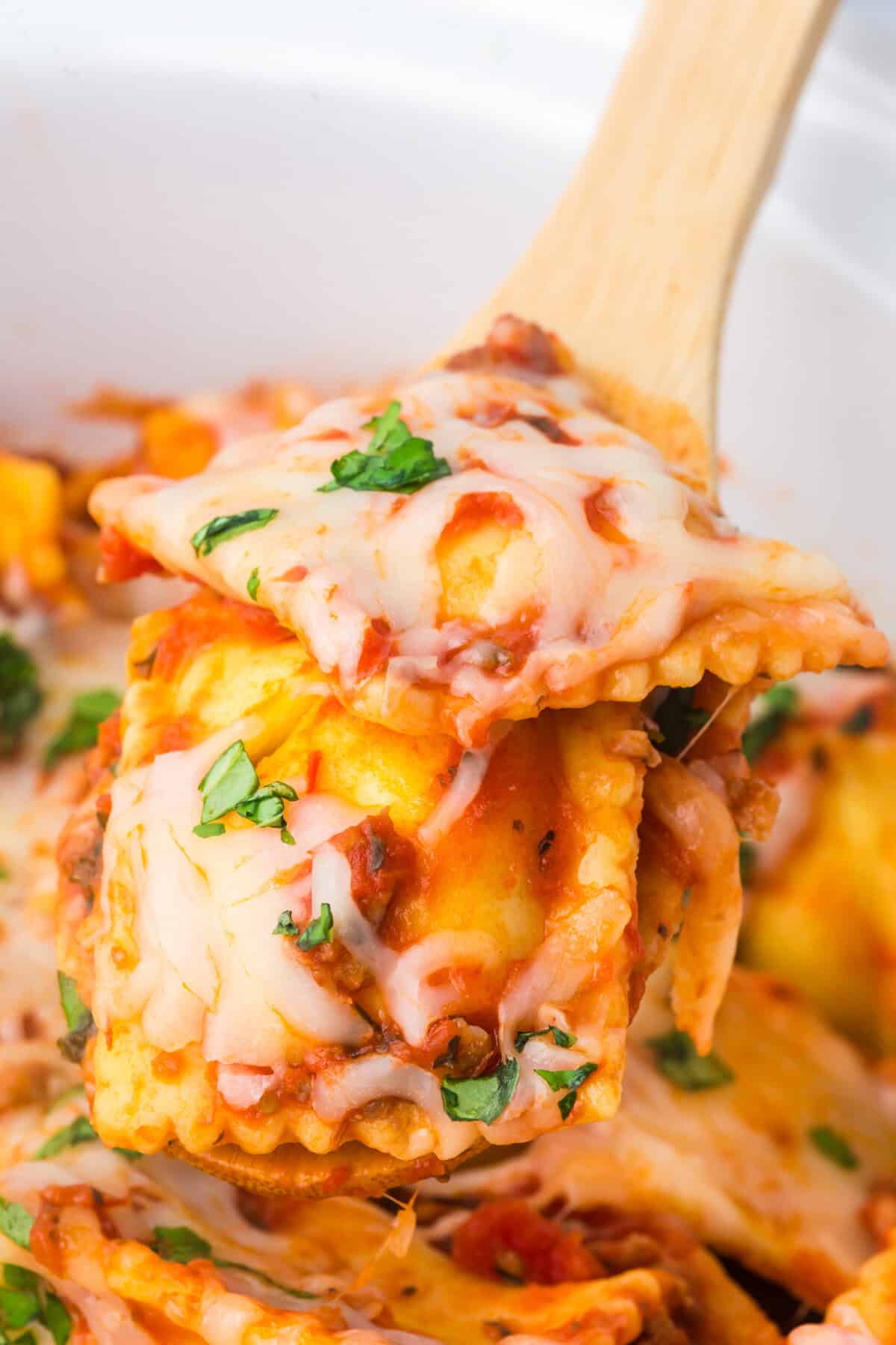A wooden spoon lifting a cheesy serving of ravioli lasagna from the slow cooker.