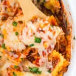 A wooden spoon lifting a cheesy serving of ravioli lasagna from the slow cooker.