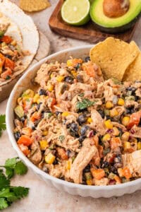 Southwest chicken salad in a white bowl with a tortilla chip, avocado and lime in the background.