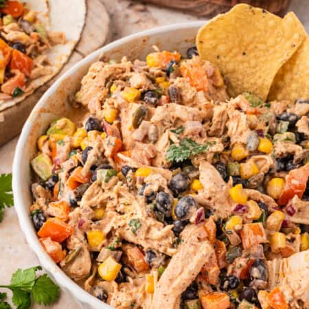 Southwest chicken salad in a white bowl with a tortilla chip, avocado and lime in the background.