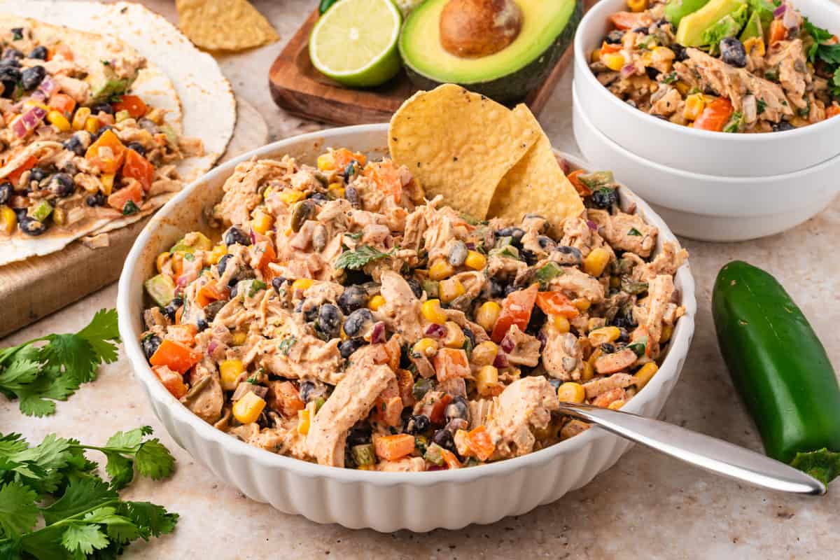 Southwest chicken salad in a white bowl with avocado and lime in the background.