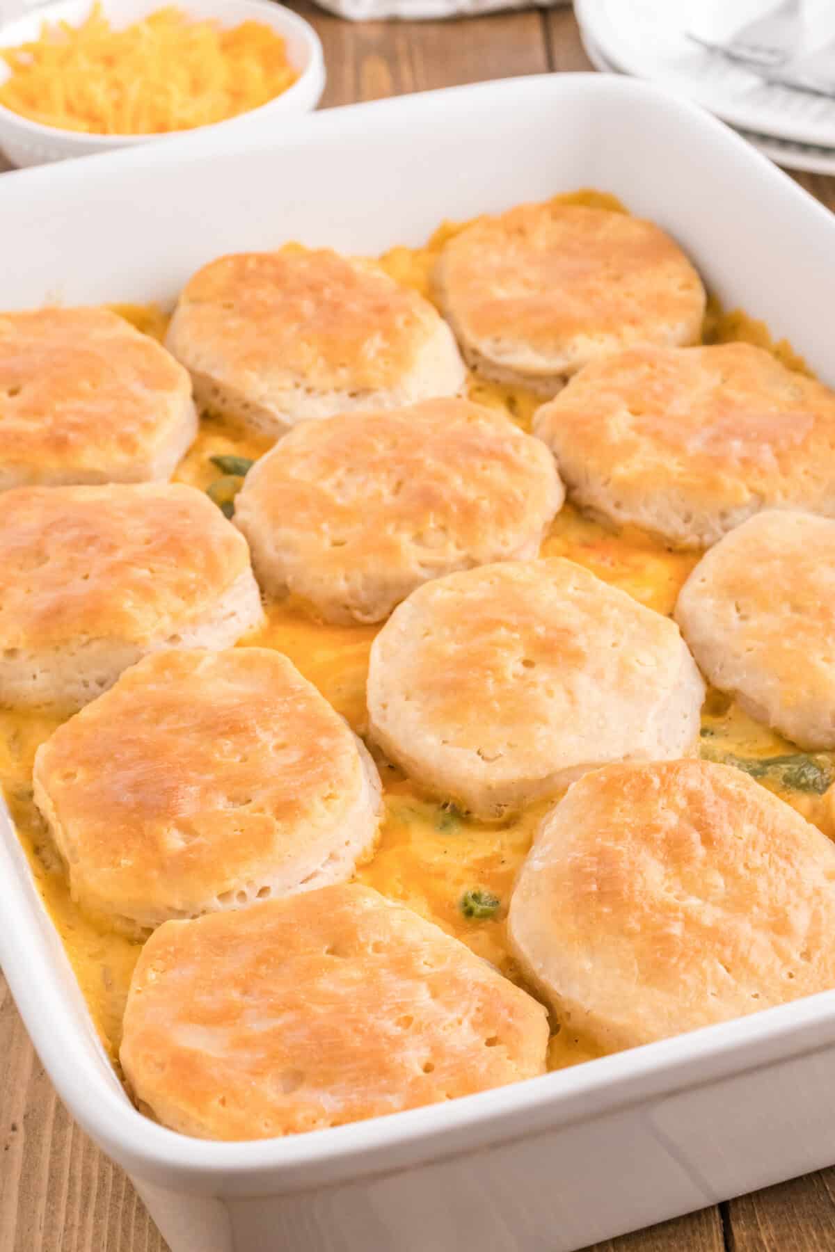 Easy chicken pot pie casserole in a white baking dish with a bowl of shredded cheddar behind it.