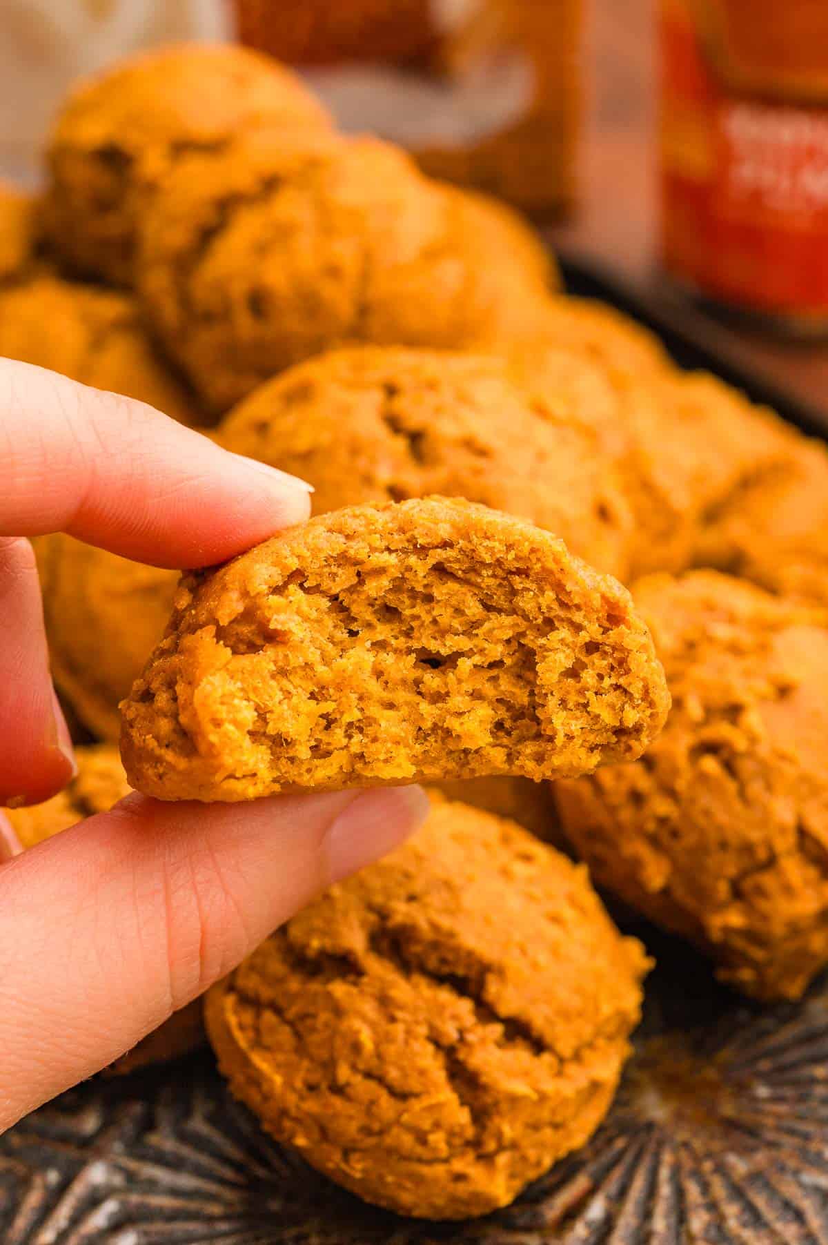 A hand holding a pumpkin cookie with a bite taken out, showing the soft cakey inside.
