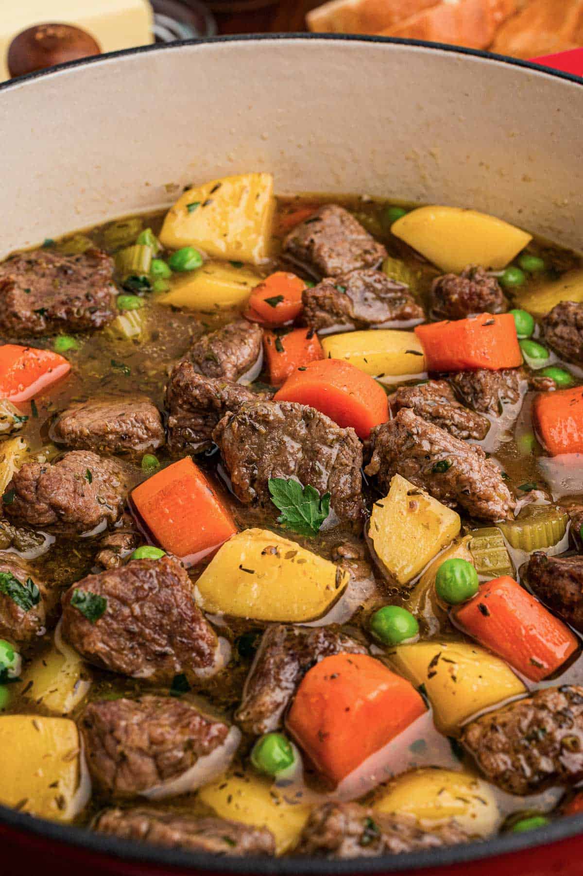 Close-up of beef stew in a pot with chunks of beef, carrots, potatoes, peas, and parsley.