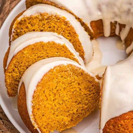 Overhead view of four glazed pumpkin cake slices fanned across a white plate.