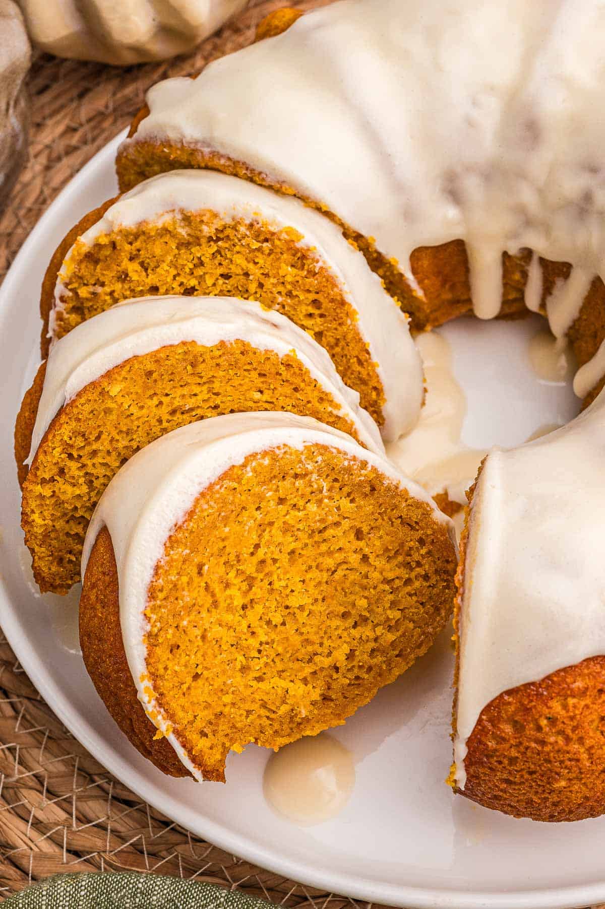 Overhead view of four glazed pumpkin cake slices fanned across a white plate.