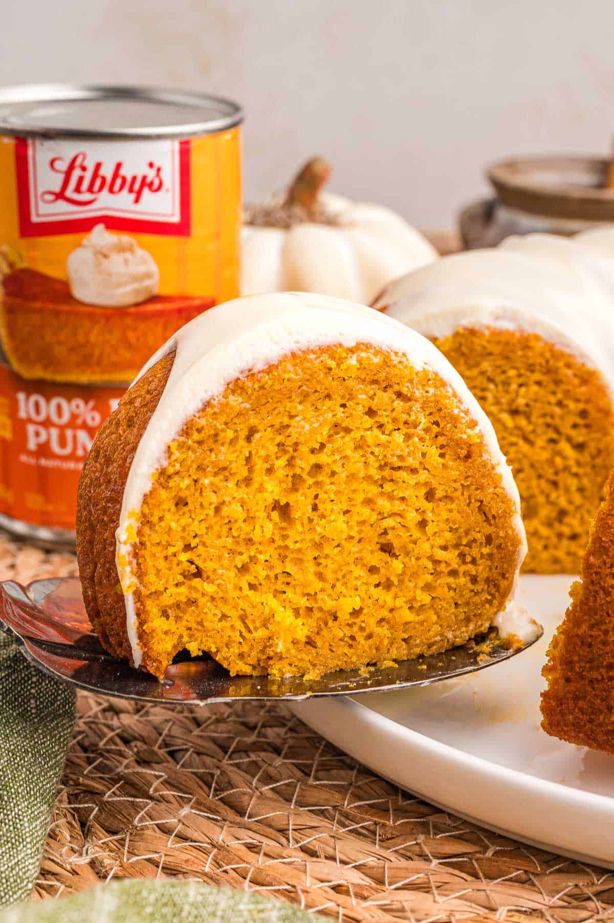 A glazed slice of pumpkin cake lifted on a cake server with a can of Libby's pure pumpkin behind it.