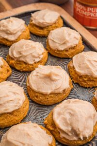 Pumpkin cookies with cinnamon cream cheese frosting on a tray.