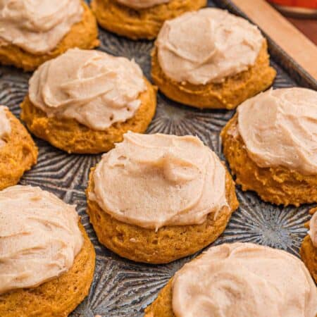 Pumpkin cookies with cinnamon cream cheese frosting on a tray.