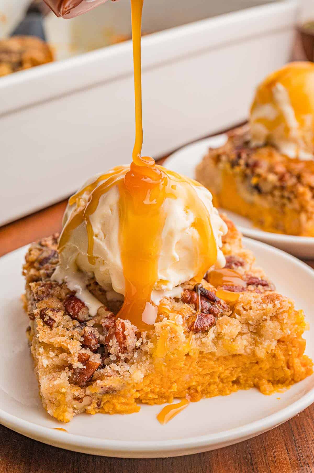 Caramel sauce being poured over a scoop of vanilla ice cream on a square of pumpkin cake.