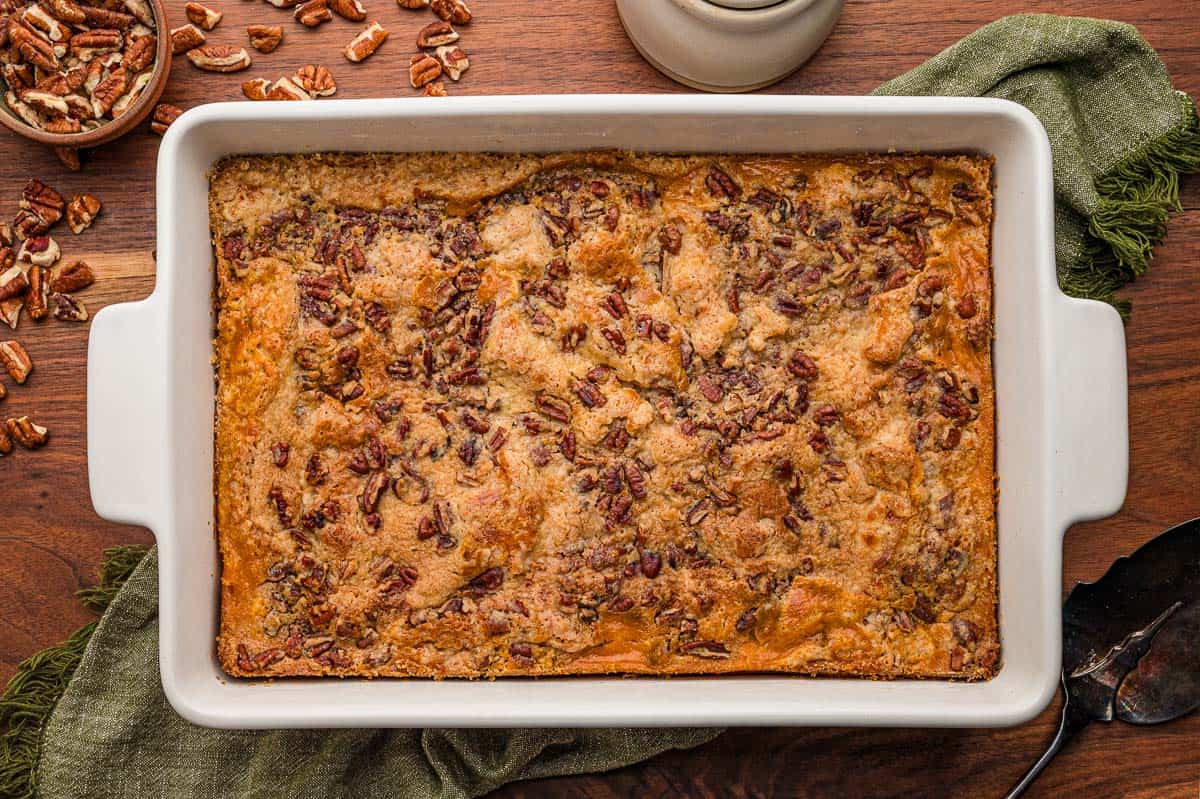 Pumpkin dump cake baked in a white 9x13 dish with a pecan topping, a green napkin and pecans alongside.