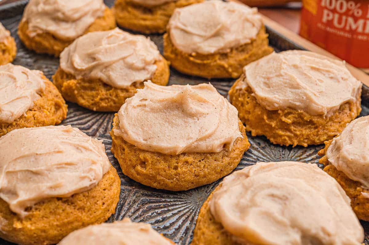 Pumpkin cookies with cream cheese frosting on a patterned metal tray with a can of pumpkin behind.