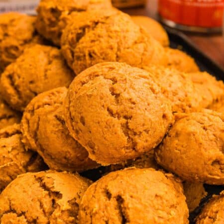 A pile of pumpkin cookies on a dark tray with a spice cake box and pumpkin can behind.