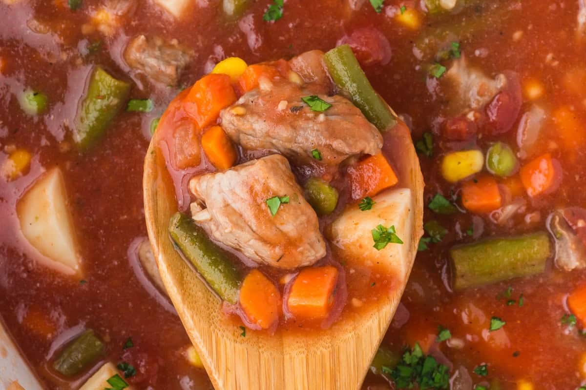 Overhead view of vegetable beef soup with chuck roast and a wooden spoon.
