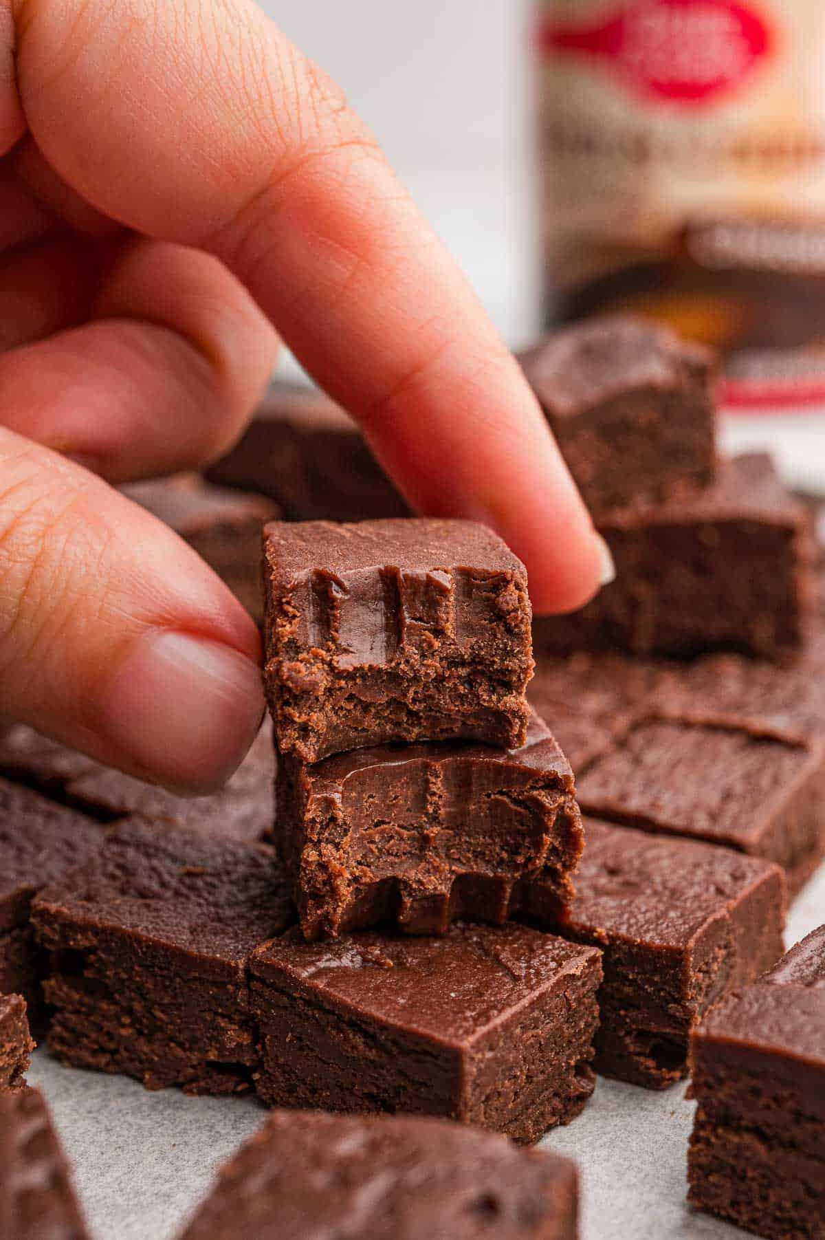 Hand holding a piece of fudge with a bite taken out over a pile of cut fudge squares.