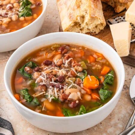 Bowl of slow cooker bean soup topped with Parmesan, with crusty bread, a block of Parmesan, and another bowl of soup beside it.